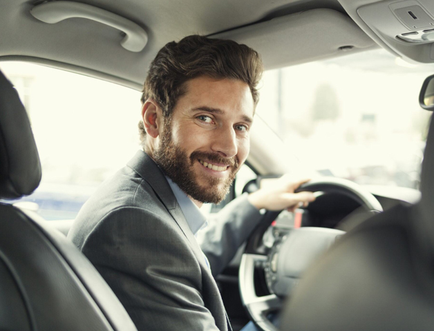 A professional driver smiling inside a car, promoting confidence and a positive road safety culture while driving for work.