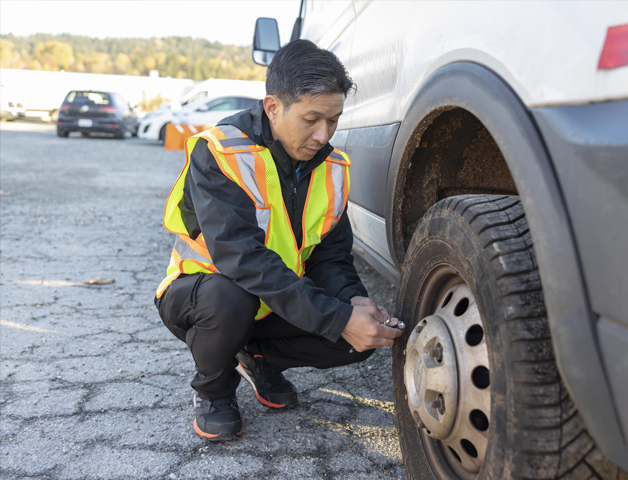 A worker in a high-visibility vest checking the tire pressure of a fleet vehicle, reinforcing the importance of vehicle inspections and understanding workplace safety rights.